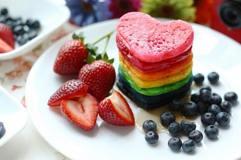 stack of rainbow colored pancakes blueberries, strawberries